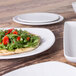 A close up of an Elite Global Solutions Tenaya off white melamine plate with a flatbread with vegetables on it.