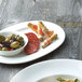 A white Chef & Sommelier bone china oval platter with a plate of food, including olives, salami, and vegetables.