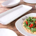 An off white rectangular melamine plate with a flatbread, red peppers, and greens on it.