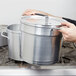 A person using a Vollrath aluminum inset in a large silver pot on a stove.