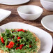 An off white Elite Global Solutions Tenaya melamine bowl on a wood surface with pizza and salad in it.