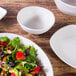 An off white Elite Global Solutions Tenaya melamine bowl on a wood surface with salad in it.