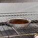 A brown cake in a D&W Fine Pack shallow foil cake pan on a rack.
