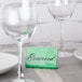 A table with a Tablecraft green melamine table tent and empty wine glasses.