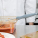 A person in a white coat using a Vollrath Spoodle to serve food from a glass container.