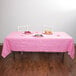 A table set with Creative Converting candy pink table cover with plates of food on it.