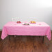 A table with a Candy Pink Creative Converting table cover and plates of food on it.