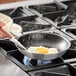 A person cooking a sunny side up egg in a Choice aluminum non-stick frying pan.
