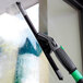 An Unger ErgoTec Ninja aluminum squeegee channel with a black and green handle cleaning a window.