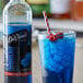 A blue drink with ice and a straw next to a bottle of DaVinci Gourmet Classic Blue Raspberry Flavoring Syrup.