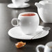 A white Chef & Sommelier bone china coffee cup on a saucer with a spoon and a cup of tea.