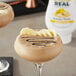 A brown drink with chocolate and banana slices in a glass on a table.