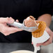 A hand using a Zeroll aluminum ice cream scoop to put ice cream in a waffle cone.