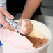 A person using a Zeroll aluminum ice cream scoop to scoop ice cream into a tub.