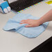 A hand wiping a surface with a blue Rubbermaid microfiber cloth.