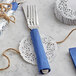 A silver fork and knife wrapped in blue paper on a silver foil lace doily.