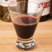 A Libbey Cosmopolitan wine glass filled with dark liquid on a table next to a bottle of wine.