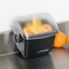 A black San Jamar Mini Dome condiment container on a counter with a clear cover next to oranges.