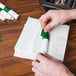 A hand using a green customizable paper napkin band to fold a white napkin.