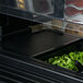 A black Cambro Versa Well cover on a counter with a container of greens inside.
