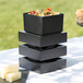 A stack of black Cal-Mil melamine boxes with food in them on a table.