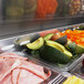Trays of food on a Turbo Air refrigerated sandwich prep table with sliced avocado and orange bell peppers.