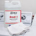 A white plastic container of Noble Chemical Break 1 with a red label next to a white towel.