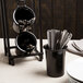 A black Cal-Mil solid melamine flatware cylinder with silverware in it.