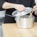 A person using a Vollrath Arkadia silver sauce pan to stir a pot with a wooden spoon.
