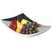 A Vollrath stainless steel curved platter with a bowl of fruit on it.
