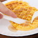 A person holding a Dart white plastic knife over waffles.