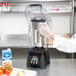 A person using a Waring commercial blender on a kitchen counter.