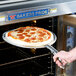 A person using a Thunder Group pizza pan gripper to remove a pizza from the oven.