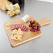 A Tablecraft wooden bread and charcuterie board with cheese, grapes, and meat on it.