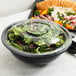 A black Fineline PET plastic bowl filled with salad and a platter of food.