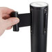 A person holding a black Aarco crowd control stanchion cylinder with a black strap.