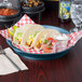 A round blue polypropylene deli server filled with tacos on a table.