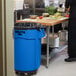 A man standing in a school kitchen next to a blue Rubbermaid Brute trash can.