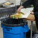 A person cutting food on a cutting board on top of a Rubbermaid Blue Brute trash can.
