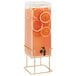 A Cal-Mil square glass beverage dispenser with orange slices in the infusion chamber on a brass wire base.