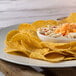A plate of Mission yellow round corn tortilla chips with a bowl of dip.