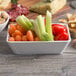 An American Metalcraft shallow rectangular melamine bowl filled with vegetables and snacks on a table.