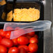 A tray of tomatoes and cheese with plastic containers and Sabert clear plastic tongs on a counter in a salad bar.