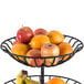 A two-tier wrought-iron basket with a bowl of apples and oranges.