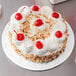 A white round cake on a white Enjay cake drum with whipped cream and cherries on top.