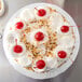 A white Enjay round cake drum under a cake with whipped cream and cherries on top.