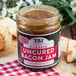 A jar of TBJ Gourmet Classic Uncured Bacon Jam on a table with food.