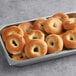 A metal tray filled with Original Bagel New York Style Plain Bagels on a table in a bakery display.