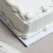 A white frosted cake on a white Enjay square cake drum.