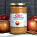 A jar of Kime's sweetened cinnamon applesauce on a table with apples and cinnamon.